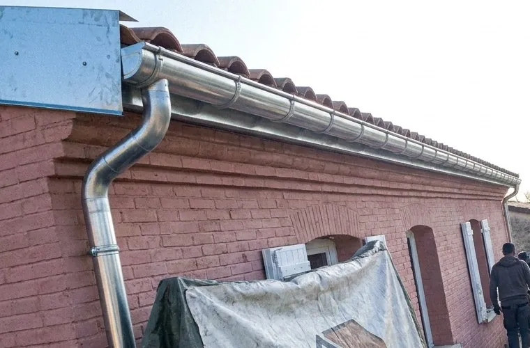 Gouttière et descente en zinc neuves sur une façade en brique rose à Castanet-Tolosan, sous un toit en tuiles canal
